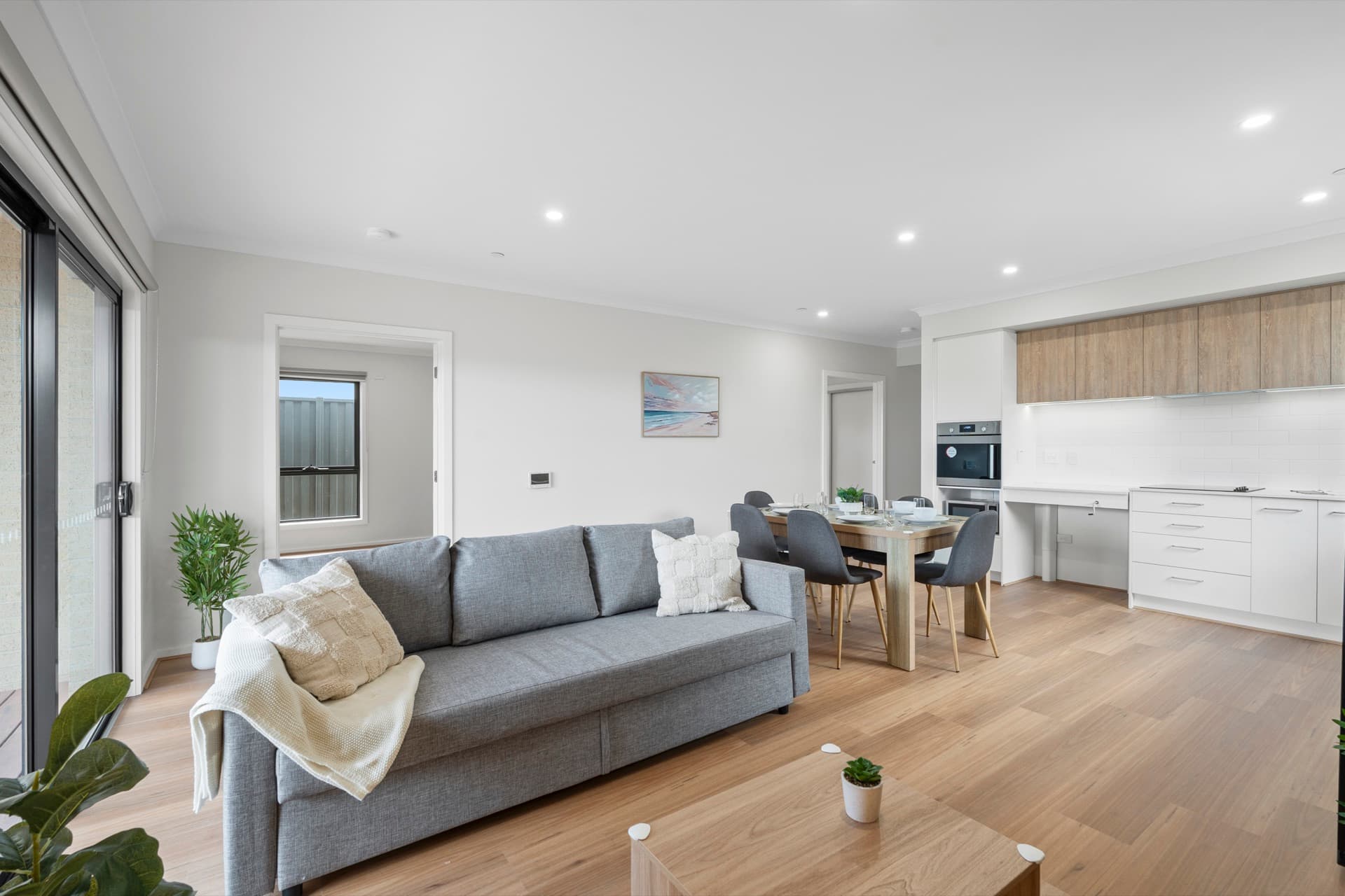 Spacious open plan living with grey sofa, throw blanket, dining setting, and modern kitchen behind