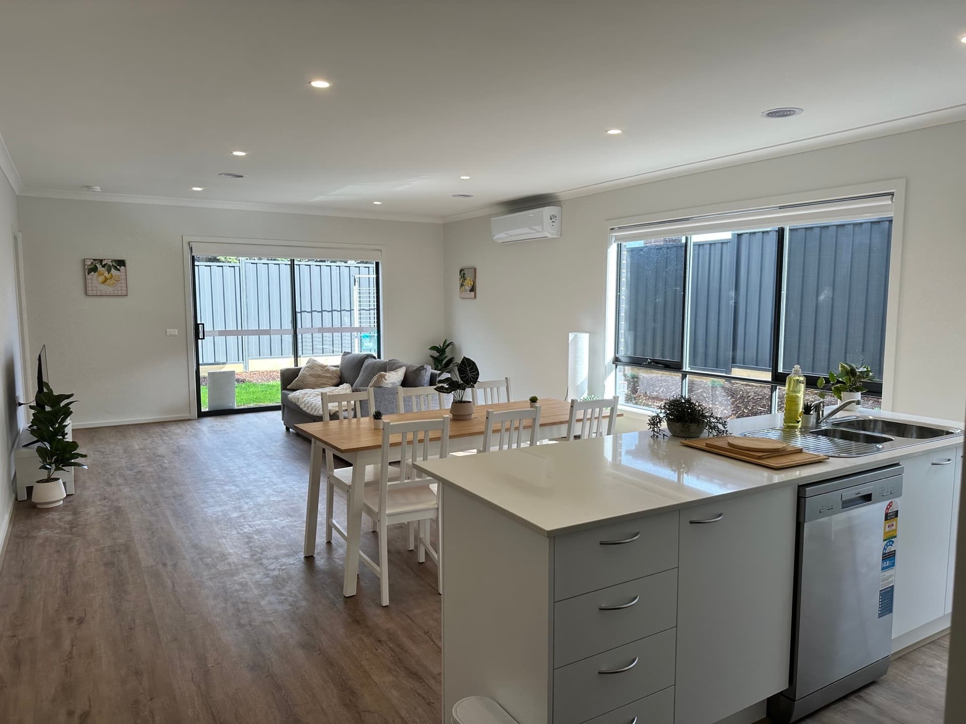 Open plan kitchen with island bench, white dining chairs, and living area visible in the background
