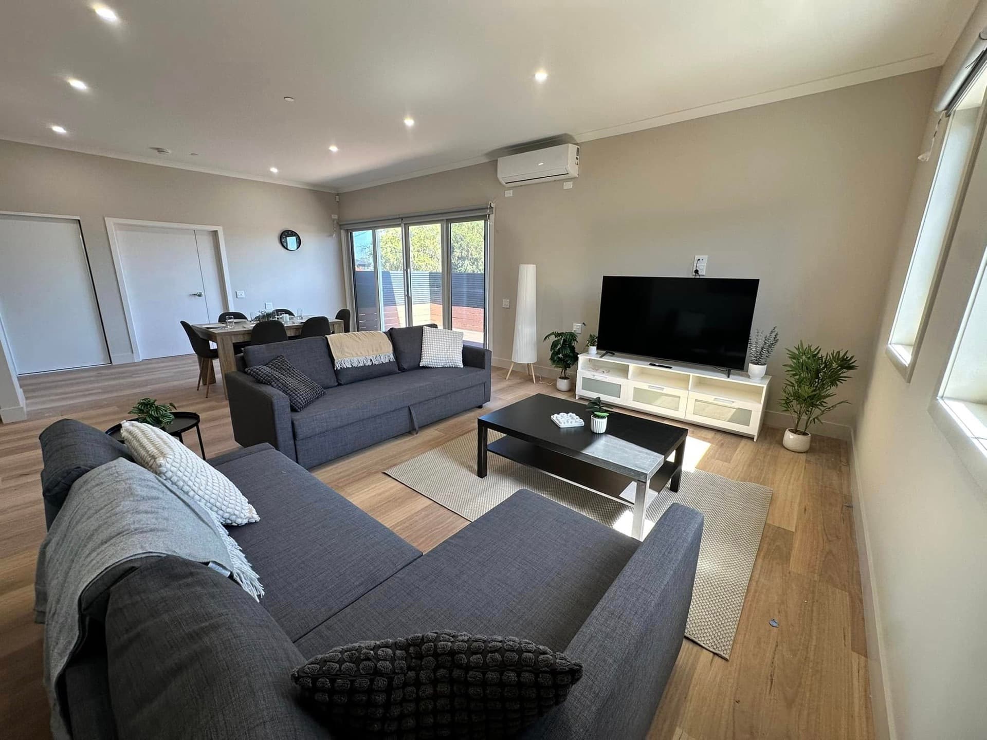 Large living room with two dark grey sofas, black coffee table, TV unit, and warm timber flooring