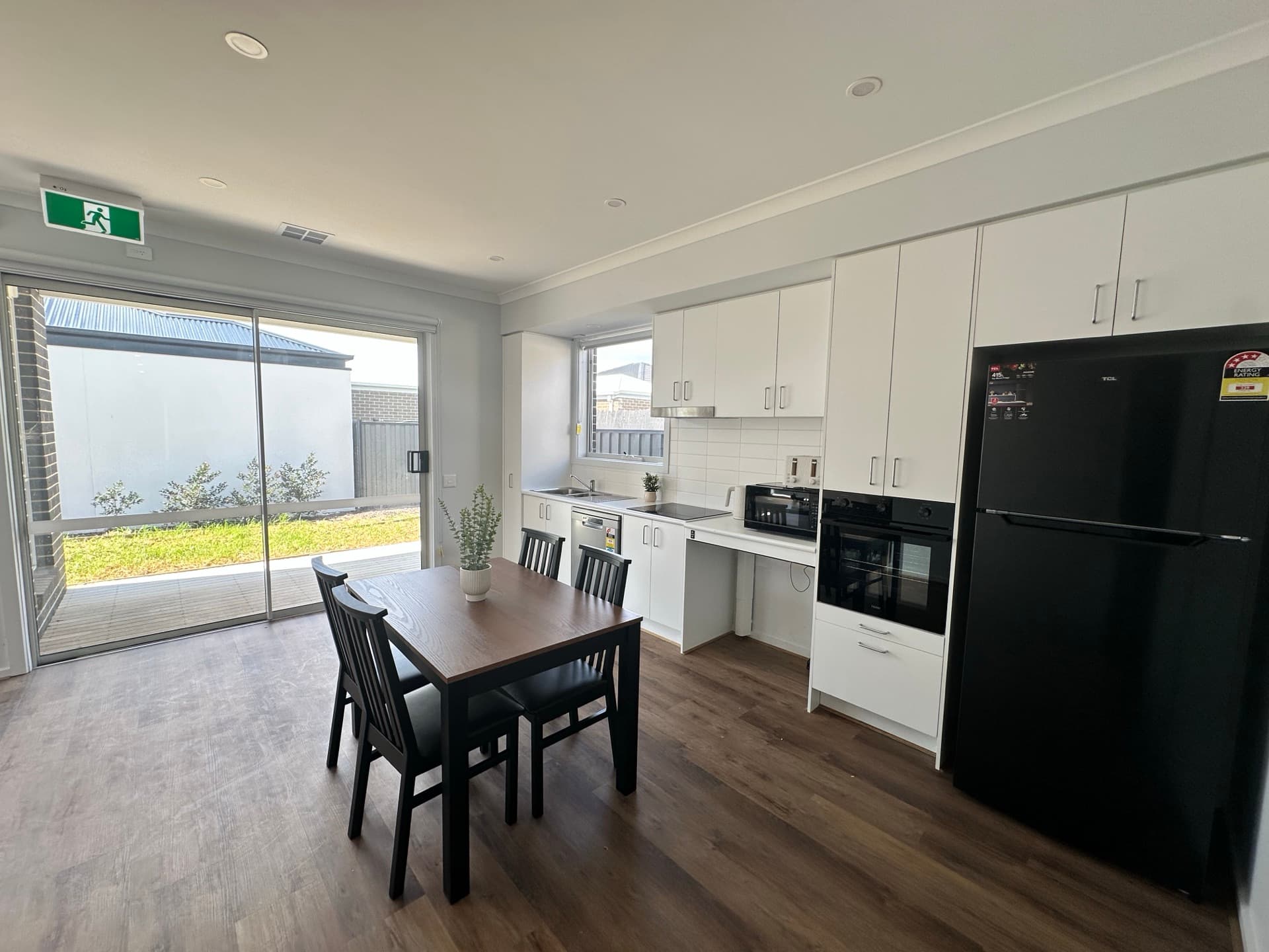 Kitchen with white cabinetry, built-in oven, dark dining table, and glass sliding door to paved courtyard